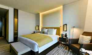 Et moderne hotellrom med en dobbeltseng, to nattbord og en komfortabel lenestol. (AI-generert tekst)