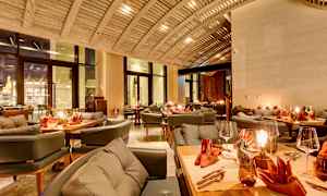 En elegant restaurant med bjelketak, dekkede bord med oransje servietter og koselig belysning. (AI-generert tekst)