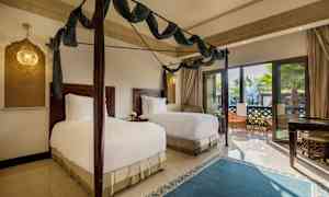 Et soverom med to enkeltsenger, mørke tremøbler og store glassdører med utsikt mot en terrasse. (AI-generert tekst)