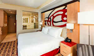 Et moderne hotellrom med en stor seng og en gjennomsiktig glassparti mot et bad. (AI-generert tekst)