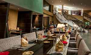 En elegant restaurant med bord oppdekket med servietter og tallerkener, samt en trapp i bakgrunnen. (AI-generert tekst)