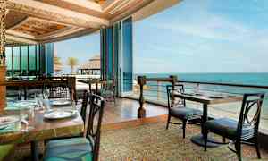 En restaurant med utsikt over havet, med glassvegger og elegante bordoppdekninger. (AI-generert tekst)