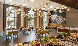 En elegant restaurant med moderne hengende lamper, dekkede bord og store vinduer som slipper inn naturlig lys. (AI-generert tekst)