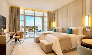 Et hotellrom med to enkeltsenger, skrivebord, lenestol og balkong med utsikt over omgivelsene. (AI-generert tekst)