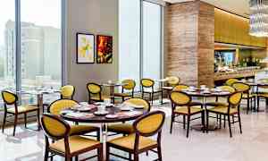 Bilde av en lys og moderne restaurant med runde bord, gule stoler og et godt utstyrt bufféområde. (AI-generert tekst)