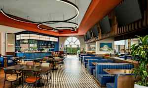 En restaurant med bord, stoler og blå sofaer samt en bar i bakgrunnen. (AI-generert tekst)