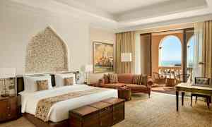 Et hotellrom med en dobbeltseng, sittegruppe, skrivebord og balkong med havutsikt. (AI-generert tekst)