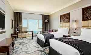 Et hotellrom med to senger, skrivebord og utsikt mot havet. Veggdekorasjon og elegant interiør. (AI-generert tekst)