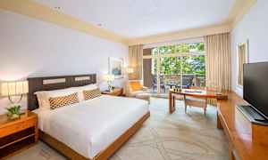 Et hotellrom med en stor seng, et skrivebord og en balkong med utsikt over grøntområder. (AI-generert tekst)