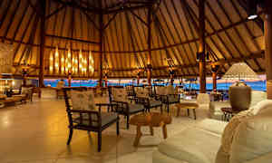 Et luksuriøst sitteområde med trestoler og sofaer, elegant belysning og en utsikt over havet gjennom åpne vegger. (AI-generert tekst)