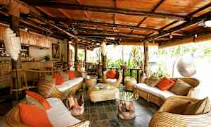 Et tropisk innredet sittegruppe med kurvmøbler og oransje puter. (AI-generert tekst)