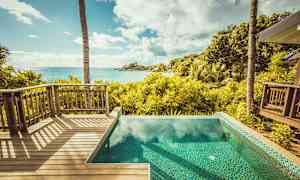 Utsikt fra en treterrasse og et basseng over en tropisk hage og havet. (AI-generert tekst)