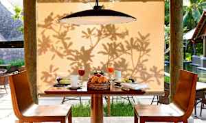 Et dekket bord med frokostmat og drikke foran en beige bakgrunn med skygge fra løv. (AI-generert tekst)