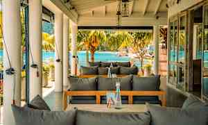 Uteservering med utsikt mot havet, møbler med grå puter. (AI-generert tekst)