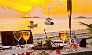 Middag på et dekket bord ved solnedgang med havet i bakgrunnen. (AI-generert tekst)