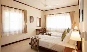 Et hotellrom med to enkeltsenger med hvite laken og dekorative sengeklær, skrivebord med speil samt store vinduer med gardiner. (AI-generert tekst)