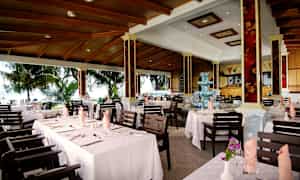 Bilde av en restaurant med dekkede bord og utsikt mot et frodig utendørsmiljø. (AI-generert tekst)