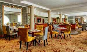 Et elegant spiseområde med flere oppdekkede bord, komfortable stoler i sennepsgul og grå farger samt dekorative søyler og speil. (AI-generert tekst)