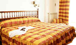 Et hotellrom med en seng med et gul og oransje rutete trekk. (AI-generert tekst)