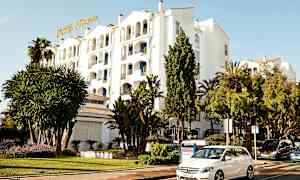 Hvit bygning med hotelskilt, omgitt av grøntområder og parkerte biler. (AI-generert tekst)