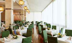 Et lyst og elegant innredet spisestueområde med grønne stoler og hvite duker på bordene, dekorert med friske blomsteroppsatser. (AI-generert tekst)