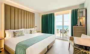 Hotellrom med stor seng og balkong med havutsikt. (AI-generert tekst)