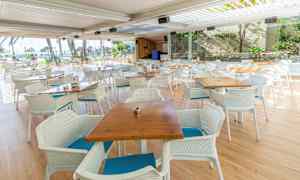 Utendørs restaurant med bord og stoler foran panoramavinduer. (AI-generert tekst)