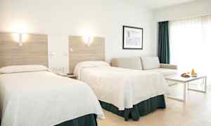 Et hotellrom med to senger, en sofa, et bord og en frokostservering. (AI-generert tekst)