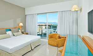 Et hotellrom med en dobbelseng, en lenestol og et glasbord. (AI-generert tekst)