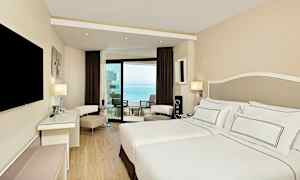 Et moderne hotellrom med en dobbeltseng og en balkong med havutsikt. (AI-generert tekst)