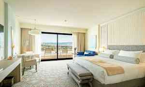 Et hotellrom med dobbeltseng, sitteområde og en balkong med utsikt. (AI-generert tekst)