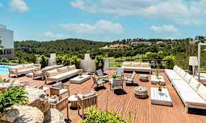 Bilde av en terrasse med hvite møbler og utsikt over et frodig landskap under en lys blå himmel. (AI-generert tekst)