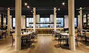 En elegant restaurant med bord og stoler samt en godt opplyst bardisk i bakgrunnen. (AI-generert tekst)