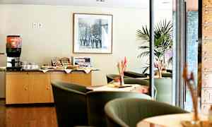 En kaffestasjon og sittegruppe på et hotell eller kafé. En kaffemaskin og snacks er plassert på et skap. (AI-generert tekst)