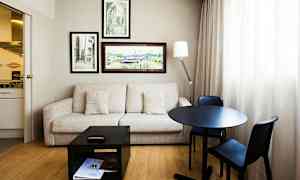 Et rom med sofa, bord og to stoler, veggdekorasjoner og et lite kjøkken. (AI-generert tekst)