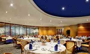 En elegant innredet spisesal med runde bord og stoler, dekorert med blå servietter og kunstverk langs veggene. (AI-generert tekst)