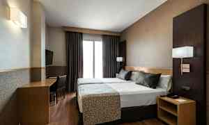Et hotellrom med to enkeltsenger som står sammen, et skrivebord med stol og en veggmontert TV. (AI-generert tekst)