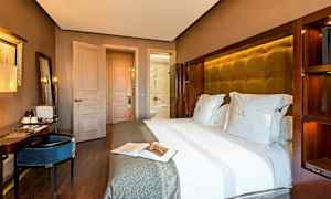 Et hotellrom med en stor seng oppredd med hvitt sengetøy, et skrivebord med sitteplass og en dør som fører til badet. (AI-generert tekst)