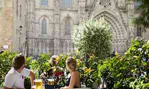 Folk sitter ved et bord omgitt av grøntområder med en praktfull bygning i bakgrunnen. (AI-generert tekst)