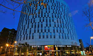 Et hotell med moderne arkitektur og en fasade med striper av glass og betong fotografert i skumringen. (AI-generert tekst)