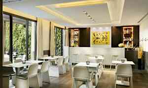 En moderne kafé med hvite bord og stoler foran en bar i en lys innredning. (AI-generert tekst)