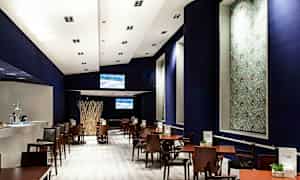 En moderne restaurant eller kafé med tremøbler og mørke dekorer. Den viser bord og stoler arrangert på rader under et sterkt opplyst tak. (AI-generert tekst)