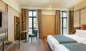 Et moderne hotellrom med to senger, et bord med en stol foran store vinduer og tregulv. (AI-generert tekst)