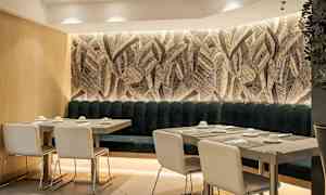 Restaurantinteriør med bord og stoler foran en vegg med bladmotiv. (AI-generert tekst)