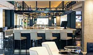 En bar i et moderne miljø med høye stoler og flasker plassert på hyller. (AI-generert tekst)