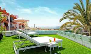 Takterrasse med gressplen, solsenger, et lite bord med drikker og utsikt over omgivelsene. (AI-generert tekst)