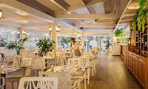 Interiør av en restaurant med treverk, hvite møbler og grønne planter. (AI-generert tekst)