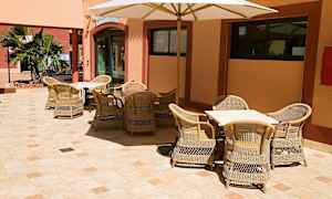 Utendørs servering med flettemøbler og en parasoll, plassert på en veranda med steingulv. (AI-generert tekst)