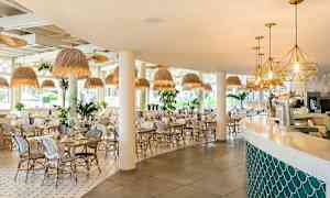 Bilde av en lys og moderne restaurant med hvite stoler og bord, hengelamper i naturnær stil, og en bar med myke linjer. (AI-generert tekst)