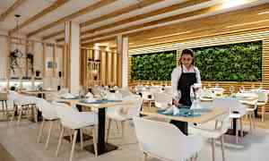 En restaurant med moderne innredning med hvite stoler, dekkede bord og en vegg dekorerte med planter. (AI-generert tekst)